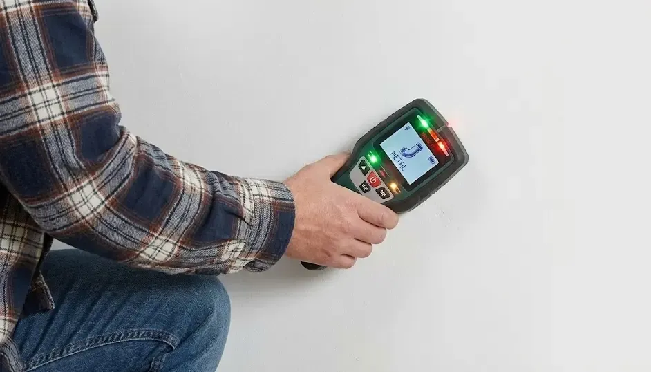 Persona usando un detector de cables y tuberías sobre una pared blanca