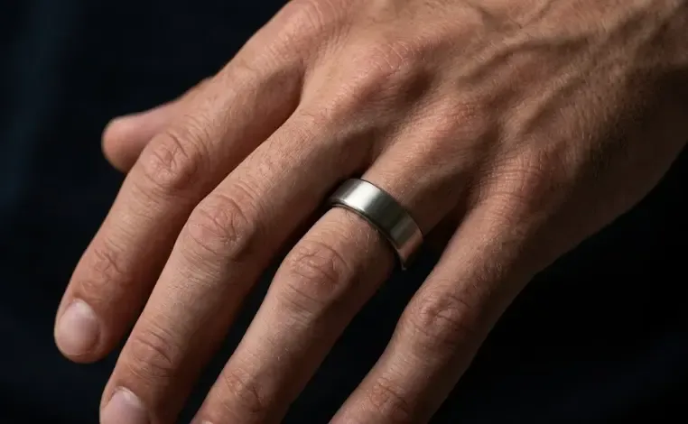 Anillo inteligente Oura Ring de titanio en mano masculina con fondo oscuro