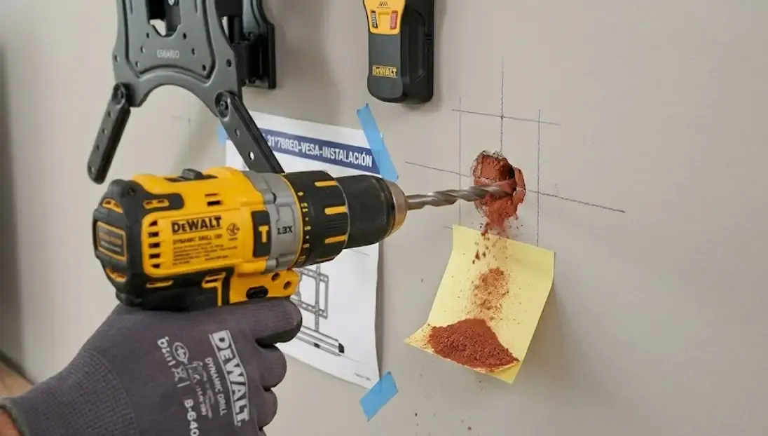 Detalle de un taladro perforando una pared con un post-it amarillo recogiendo el polvo de ladrillo rojo justo debajo